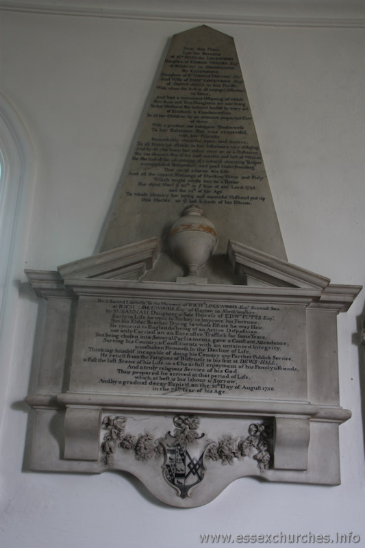 St Mary & All Saints, Lambourne Church – UPPER INSCRIPTION Near this place lye the remains of Mrs Matilda Lockwood, daughter of George Vernon Esq of Sudbury in Derbyshire; by Catherine daughter of Sir Thomas Vernon Kt, and wife of Richard Lockwood Esq of Dews-Hall in this parish: with whom she liv'd in all conjugal affection 31 years, and had a numerous offspring; of which five sons and two daughters are now living. To her husband she indear'd herself by every act of Kindness & Condescension. To all her children by an attentive, impartial care of them, with a prudent, not indulgent, tenderness to her relations she was respectful with her friends. Remarkably cheerful, open and sincere; To all mankind affable, to her inferiors very obliging and by all who knew her either near or at a Distance, she was esteem'd One of the most amiable and best of Women for she had all the advantage of a natural-charming Temper, Accomplish'd Behaviour, and good Understanding that could adorne this Life. And all the inward blessings of Christian Virtue and Piety which might intitle her to a Better. She dyed November ye 25th in ye Year of our Lord 1743 and the 54th of her Age. To whose memory her loving and mournful husband put up this Marble as ye last tribute of his Esteem. LOWER INSCRIPTION Be it Sacred Likewise, To the memory of Richard Lockwood Esq, second son of Richard Lockwood Esq of Gayton in Northamptonshire; by Susannah, daughter & sole heiress of Edward Cutts Esq. Early in life he went to Turkey to improve his fortune; But his Elder Brother Dying to whose Estate he was Heir, he return'd to England, & being of an Active Disposition, not only Carried on an Extensive Traffic for some Years, But being chosen into Several Parliaments, gave a Constant Attendance; Serving his Country & Constituents with an untainted Integrity, & unshaken Firmness, in the Decline of Life, thinking himself incapable of doing his Country any Farther Publick Service, he retir'd from the Fatigues of Busyness to his seat at DEWS-HALL; & Past the last Scene of his Life in a Chearfull enjoyment if his Family & Friends, And a truly religious Service of his God. Thus prepared he arrived at that period of Life, which at best, is but labour & sorrow, and by a gradual decay, Expir'd on the 31st day of August 1756, in the 78th Year of his age.